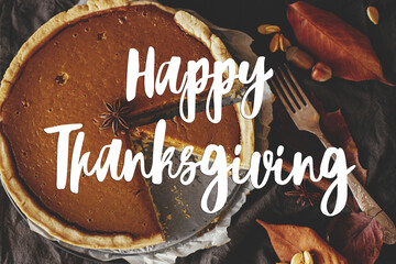 Happy thanksgiving text on pumpkin pie on rustic table with napkin, autumn leaves, spices, dinner...
