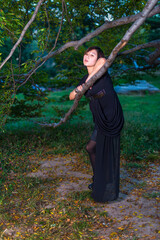 A Chinese girl, dressing in dark, is relying on a branch of a tree, mysteriously wandering in the dark of the night..