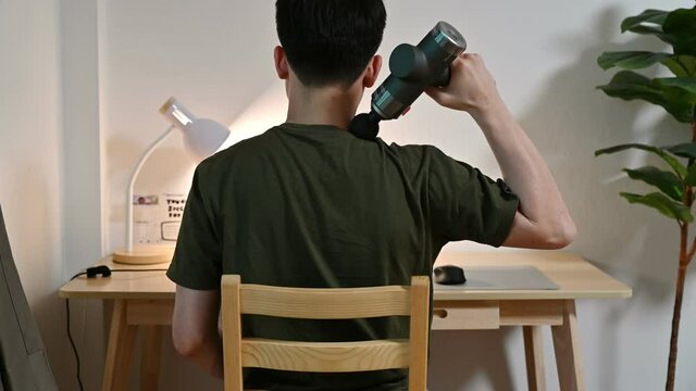 Back view of man massaging shoulder with gun massage machine