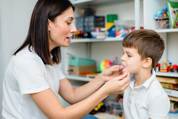 A woman speech therapist deals with a boy and does an exercise to correct the speech apparatus using a straw or spaghetti