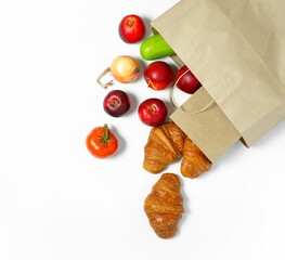 Products in a paper bag vegetables apples, onions, zucchini, tomatoes, croissants on a light background.