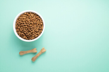 A full bowl of dry pet food and natural toothpicks. On a colored background, top view, copy space.