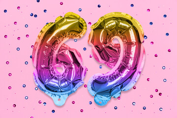 Rainbow foil balloon number, digit sixty nine on a pink background with sequins. Birthday greeting card with inscription 69. Top view. Numerical digit. Celebration event, template.