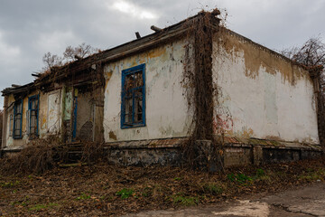 Obraz na płótnie Canvas An old crumbling servants' house, in an abandoned noble estate. A white old house, almost destroyed, overgrown with grass and grapes. An ordinary crumbling building, in an unusual place in Russia.