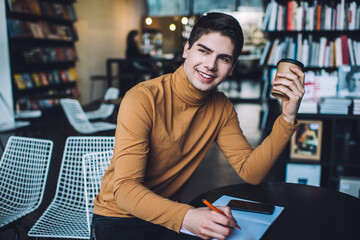 Happy young man with notebook and smartphone in library