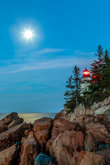Just before dawn, the light of a full moon reflects upon the sea at the Bass Harbor Head Light, a lighthouse in Acadia National Park on the southern tip of Mt. Desert Island in Down East Maine. - 468625384