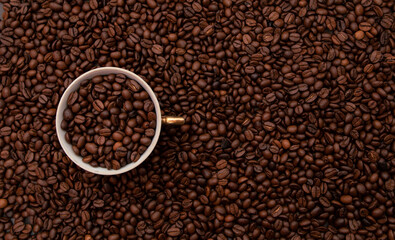 White Cup  full of coffee beans. With a lots of beans around. Coffee background. Beautiful vintage mug, cup.