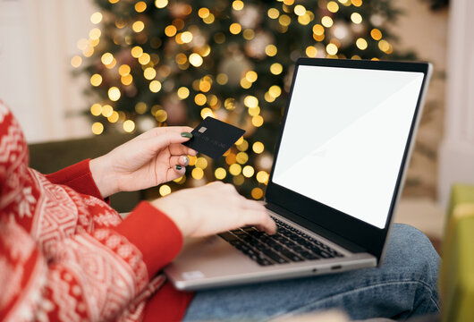 Christmas online shopping, sales and discounts promotions during winter holidays, online shopping at home. Mock-up. Female hands on the laptop with credit card and blurred bokeh lights