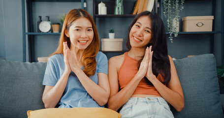 Teenager couple Asian women feeling happy smiling and looking to camera while relax in living room at home. Cheerful Roommate ladies video call with friend and family, Lifestyle woman at home concept.