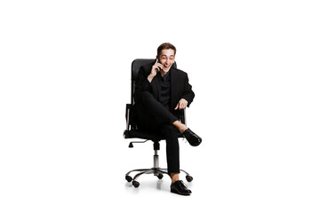 Portrait of young man in black business suit, office manager sitting on chair isolated on white background. Art, inspiration concept.