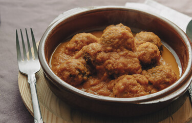 Rustic plate of meatballs in tomato sauce set on a tablecloth.