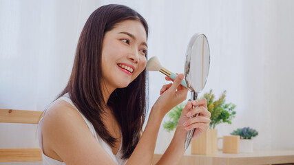 Asian woman using powder by brush make up in front mirror, Happy female using beauty cosmetics to...