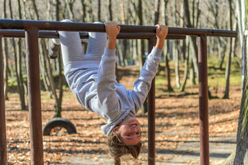Fototapeta premium Little adorable girl child in a tracksuit trains on horizontal bars on the street in the autumn forest