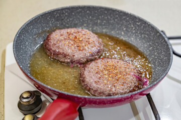 Juicy minced beef patties are fried in oil in a frying pan on a gas stove