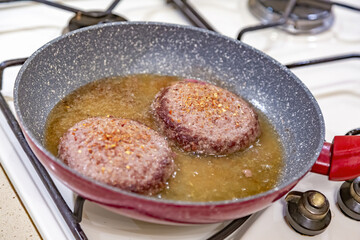 Juicy minced beef patties are fried in oil in a frying pan on a gas stove
