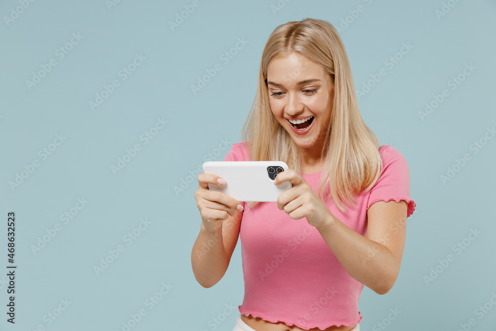 Wall mural young excited blonde woman 20s wearing casual pink t-shirt using play racing app on mobile cell phon