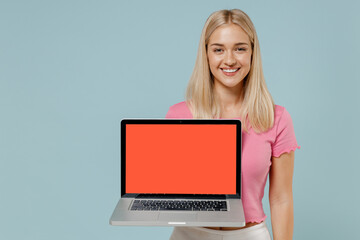 Naklejka premium Young smiling happy caucasian blonde woman 20s wear casual pink t-shirt hold use work on laptop pc computer blank screen workspace area isolated on plain pastel light blue background studio portrait