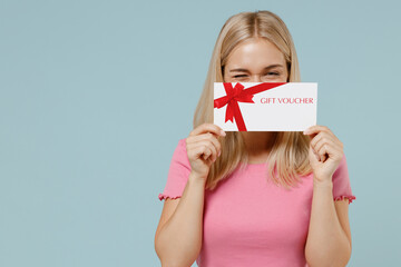 Full body fun young blonde woman 20s wearing casual pink t-shirt sit in bag chair cover mouth with gift certificate coupon voucher card for store isolated on plain pastel light blue background studio. - obrazy, fototapety, plakaty