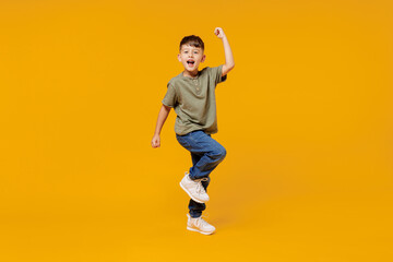 Full body little small fun happy boy 6-7 years old wearing green t-shirt do winner gesture clench fist isolated on plain yellow background studio portrait. Mother's Day love family lifestyle concept. - obrazy, fototapety, plakaty