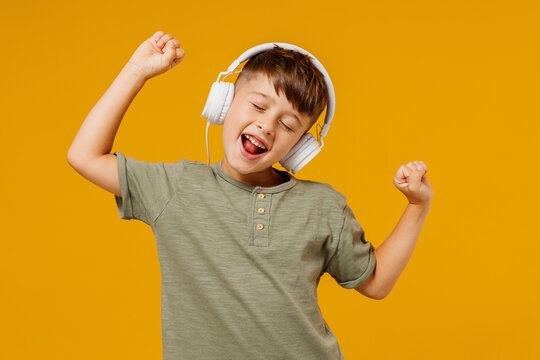 Little small cheerful happy boy 6-7 years old wearing green t-shirt headphones listen to music dance isolated on plain yellow background studio portrait. Mother's Day love family lifestyle concept