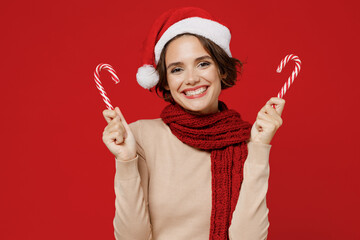 Young smiling fun happy caucasian woman 20s wear Santa Claus Christmas red hat hold candy cane stick lollipop isolated on plain red background studio portrait. Happy New Year 2022 celebration concept.