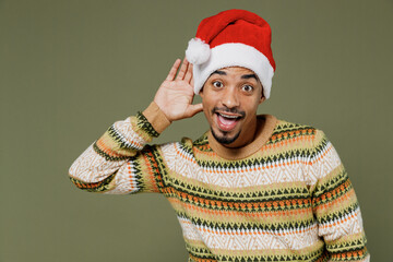 Young african man in knitted sweater red Christmas Santa Claus hat try to hear you overhear...