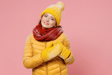 Fascinating charming magnificent joyful young woman 20s years old wears yellow jacket hat mittens look camera put folded hands on heart isolated on plain pastel light pink background studio portrait.