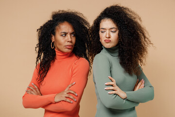 Two angry displeased upset young curly black women friends 20s wearing casual shirts clothes stand back to back look at each other swearing isolated on plain pastel beige background studio portrait. - obrazy, fototapety, plakaty