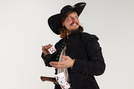 Cropped portrait of man, medeival pirate with pistol playing cards isolated over white background