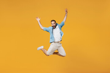 Fototapeta na wymiar Full body young smiling happy caucasian man 20s wearing blue shirt white t-shirt jump high with outstretched hands arms isolated on plain yellow background studio portrait. People lifestyle concept.