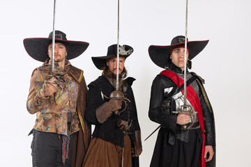 Cropped portrait of thee men in vitage costumes with swords, musketeer and pirate isolated over...