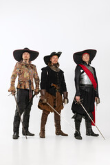 Full-length portrait of thee men in vitage costumes with swords, musketeer and pirate isolated over...