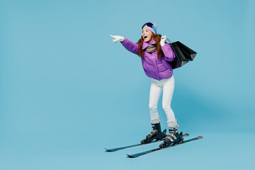 Full body skier woman in warm purple jacket ski goggles mask spend weekend in mountains holding...
