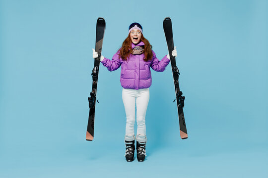 Full body skier shocked happy cheerful fun woman in warm purple padded windbreaker jacket goggles mask spend extreme weekend in mountains hld ski look camera isolated on plain blue background studio