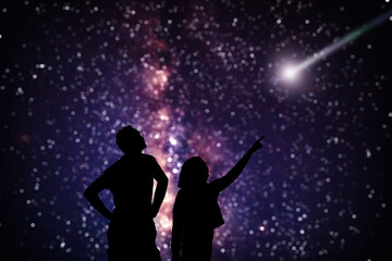 Silhouettes of father and daughter under starry skies.