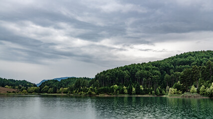 Fototapeta premium The shores of the mountain lake are overgrown with coniferous forest