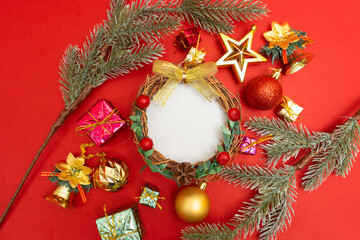 Flat lay Christmas holiday red background composition with white circular space, for mock up greetings artwork. Green and gold Christmas ornaments, presents and golden star