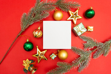 Fototapeta na wymiar Flat lay Christmas holiday red background composition with white square space, for mock up greetings artwork. Green and gold Christmas ornaments, presents and golden star