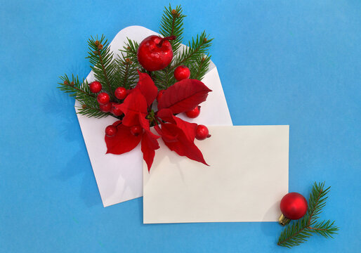 Christmas decoration. Flower of red poinsettia, christmas tree, ball, apple, red berries in postal envelope, blank sheet with space for text on a blue paper background. Top view, flat lay