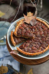 Canadian tart with pecan and maple syrup on a wooden stand. Dessert with nuts on the table with autumn leaves, plates and cutlery
