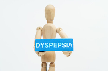 A figurine of a man holds in his hands a blue wooden block with the inscription DYSPEPSIA. The figurine is out of focus.