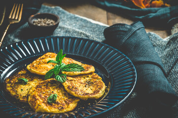 Small round pancakes with herbs on a blue plate on blue and wooden background