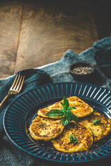 Small pancakes with herbs on a blue plate on rustic wooden background, vertical with copy space