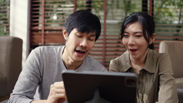 Asian couple using a tablet and laptop computer working from home in living room.