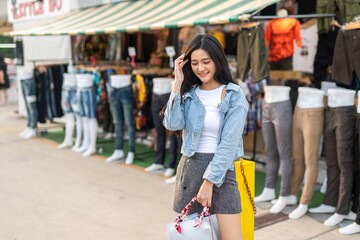 Beautiful asian female young model lady having a solo shopping and stroll walk time by herself and looking through concentratedly some fashion dresses put on sale at a fashion store in a night market 