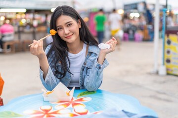 Beautiful asian female young model lady having a stroll walk relaxingly and eating delicious and tasty street food from the food bazaar in a night market happily and cheerfully