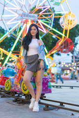 Obraz na płótnie Canvas Beautiful asian female young model lady having a stroll walk relaxingly and posing happily and cheerfully in front of some colorful night fixture led lights and playground in a night market 