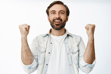Happy pleased guy fist pmps, looking at smth with relieved joyful face, smiling pleased, watching sport game, standing over white background