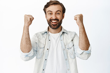 Enthusiastic bearded man say hooray, cheering and celebrating, smiling happy, achieve goal or winning, white background