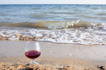 a glass of wine stands on the sand by the sea